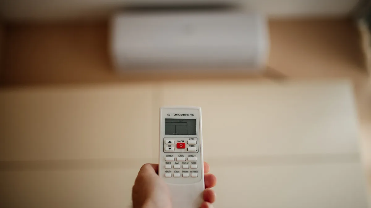 Mano con el control remoto ajustando la temperatura del aire acondicionado para ahorrar luz